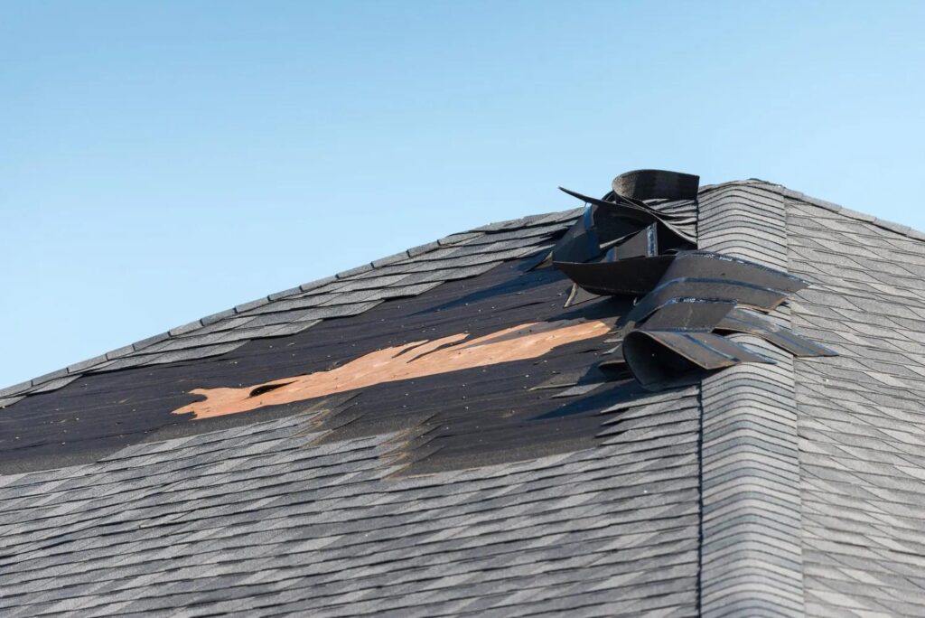 Storm-damaged roof with torn shingles near a roof vent